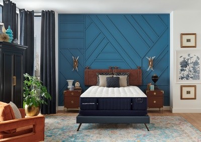 A mattress on a blue bed frame in a decorated room with a teal textured wall and patterned rug