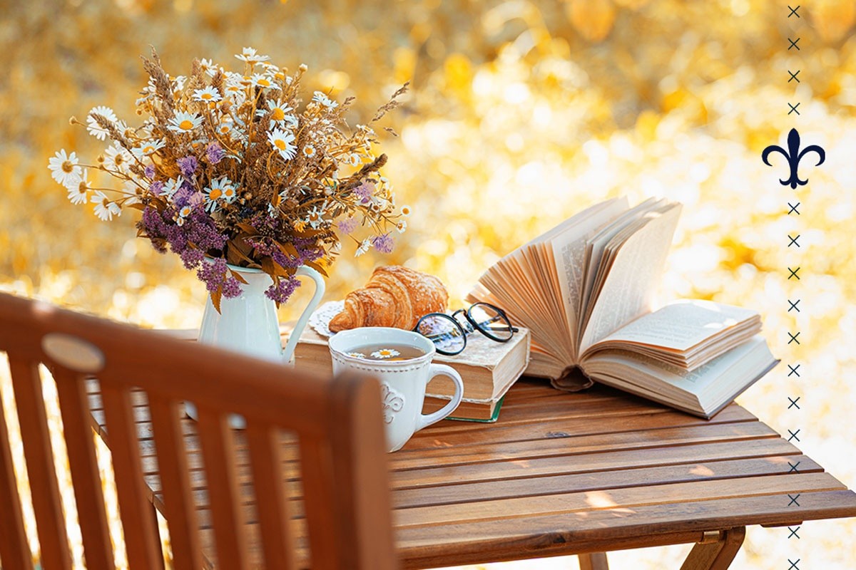 An outdoor table and chair, set up with books, flowers, and reading glasses, on a sunny day in the fall